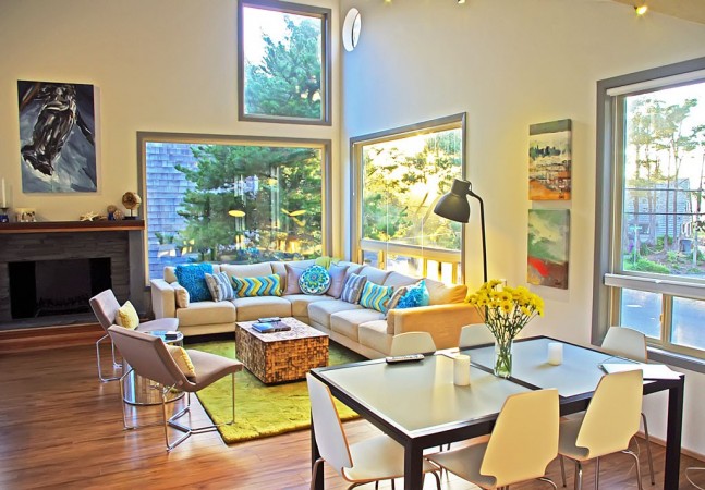 A living room with large windows and a table and chairs in an open floor plan setting.