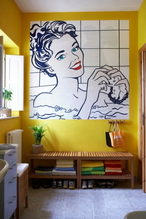 A yellow bathroom with a pop art painting of a woman.