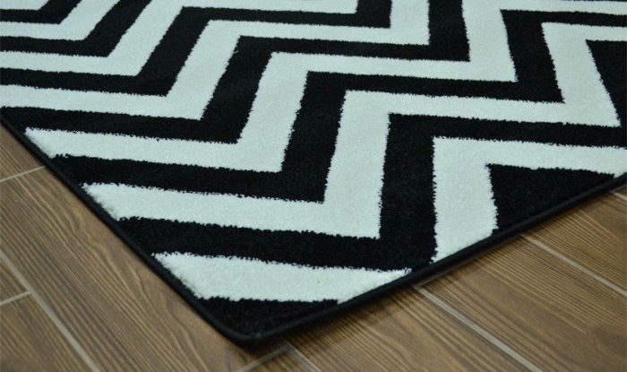 An optical art-inspired black and white chevron rug on a wooden floor.