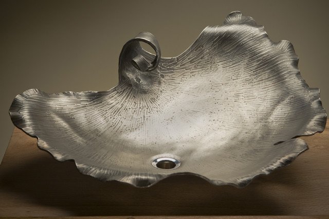 A silver leaf shaped vessel sink on top of a wooden table.