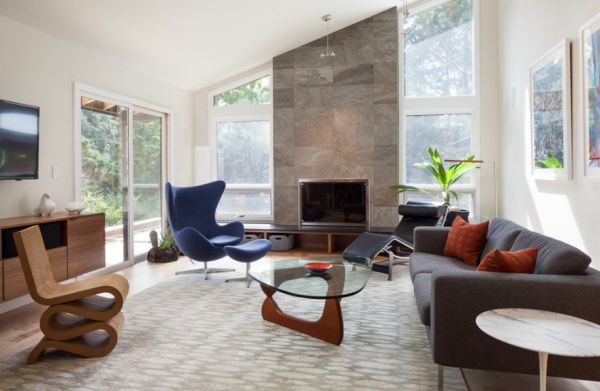A mid-century modern living room with large windows and a fireplace.