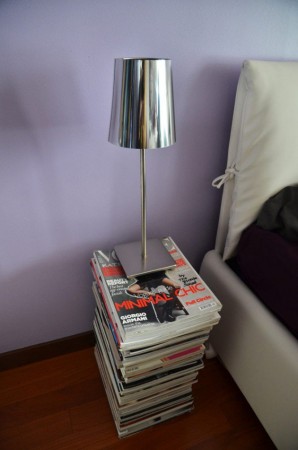 A stack of magazines on a nightstand next to a bed.