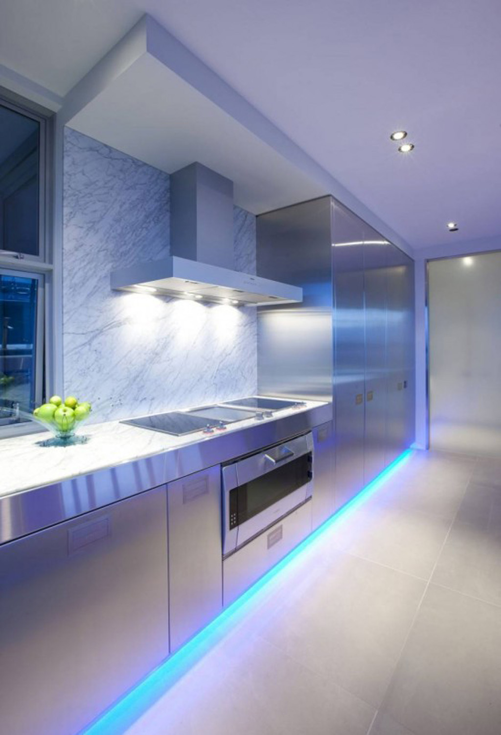A modern kitchen with blue lighting and stainless steel appliances illuminating the space.