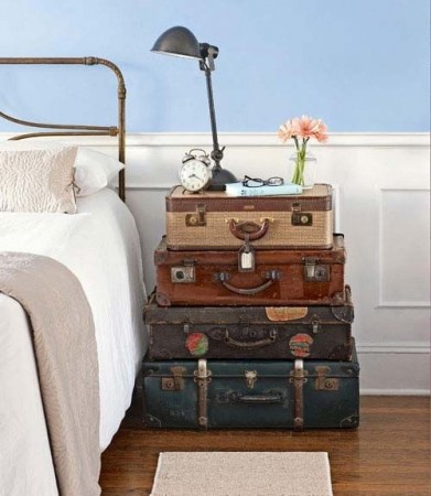 A stack of suitcases next to a bed with nightstands in a bedroom.