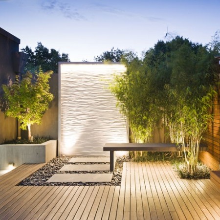 A modern backyard with a wooden deck and lighting, featuring water walls.