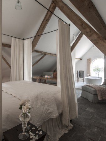 A stunning attic bedroom with a bed and a bathtub featuring exposed ceiling beams.