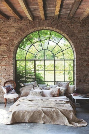 A bed in a room with a gorgeous arched window.