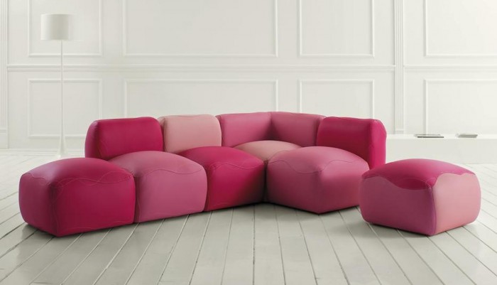 A fun and unique pink couch and ottoman in a white room.