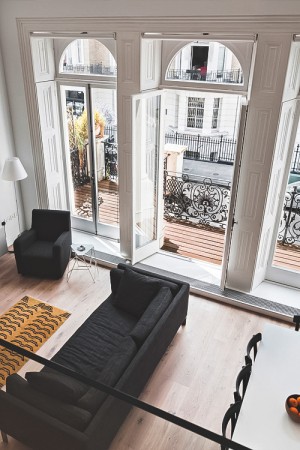 A living room with large windows overlooking the provincial Parisian neighborhood, featuring a black couch.