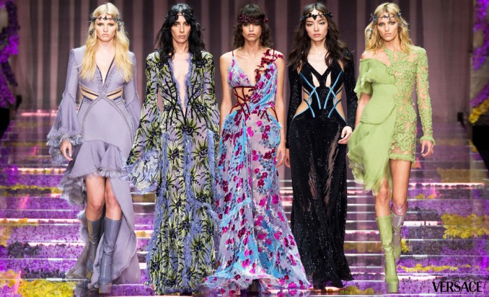 Four haute couture models walk down a runway in colorful dresses.