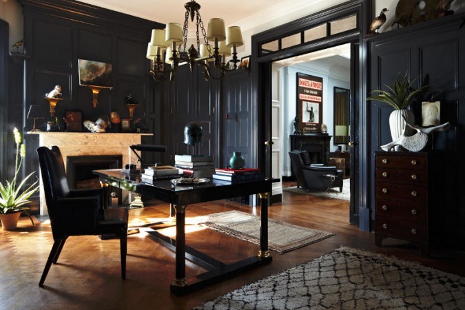 A home office with black walls and a chandelier.