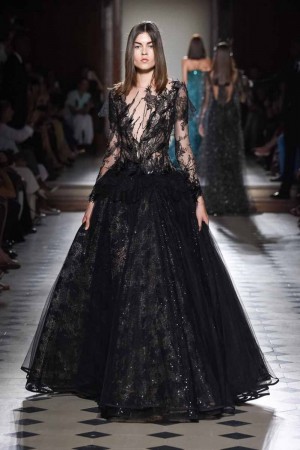 A model walks down the runway in a black gown during a haute couture fashion show.