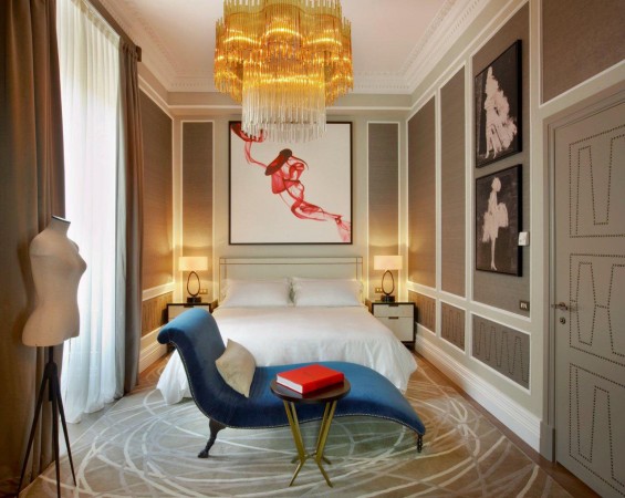 A bedroom with a bed, chair, and a painting on the wall featuring haute couture interior design.