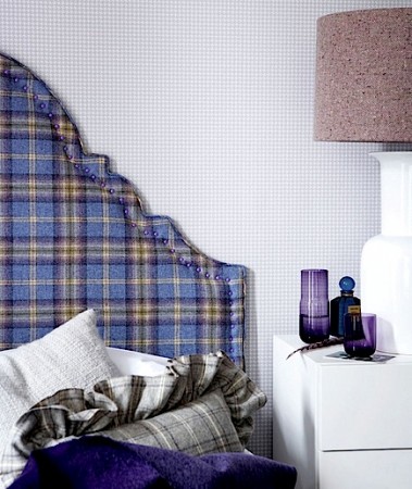 A bed with a plaid headboard and purple pillows.