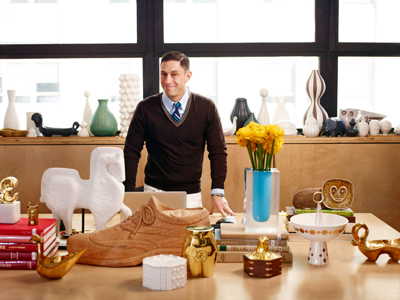 A man standing in front of a desk with a lot of Jonathan Adler vases.