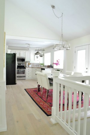 A white kitchen with a wooden railing and a rug transformed by painted white floorboards.