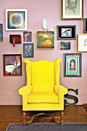 A yellow chair in front of a wall of framed pictures adds bold neon hues to your home decoration.