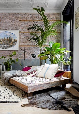 A room with a bed and plants in front of a brick wall, creating a Tropical Paradise.