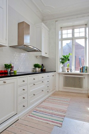A kitchen with white cabinets and painted white floorboards.