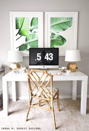 A white desk with two framed pictures and a chair, creating a tropical paradise at home.