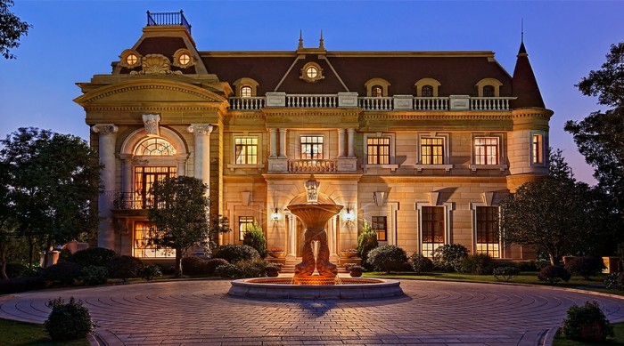 A luxurious mansion with a fountain in front of it.