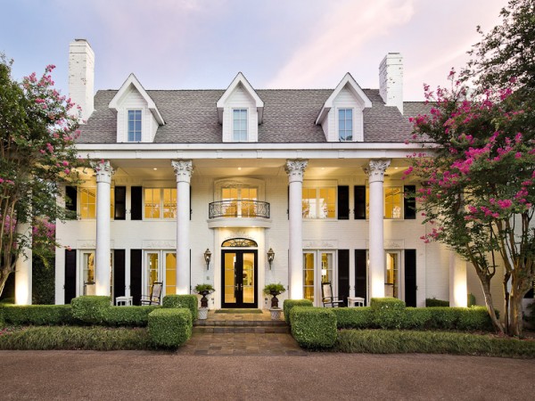 A large luxury white house with columns and amenities such as bushes.