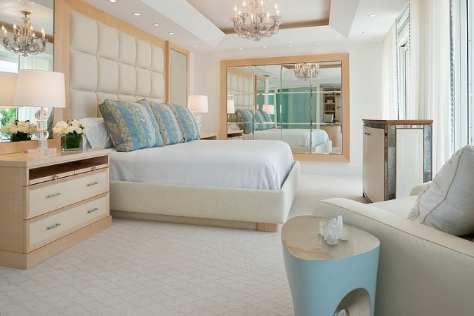 A bedroom with a large bed and a bold chandelier in Beautiful Palm Beach style.