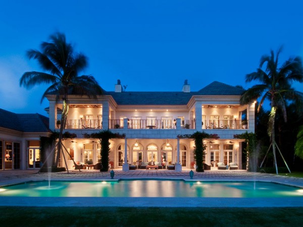 A bold and beautiful mansion with a pool, adorned with palm trees in Palm Beach style.