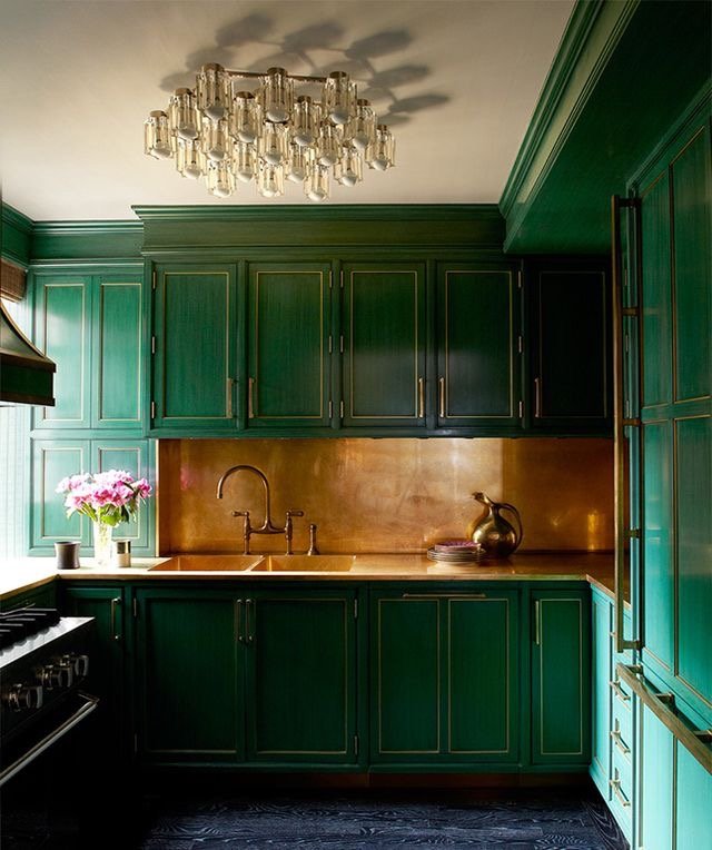 A glamorous kitchen with emerald green cabinets and a gold chandelier.