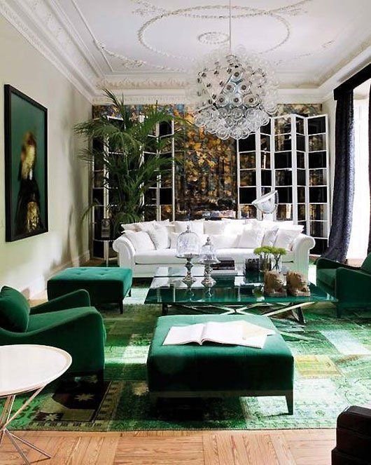 A glamorous living room with emerald green furniture and a chandelier.