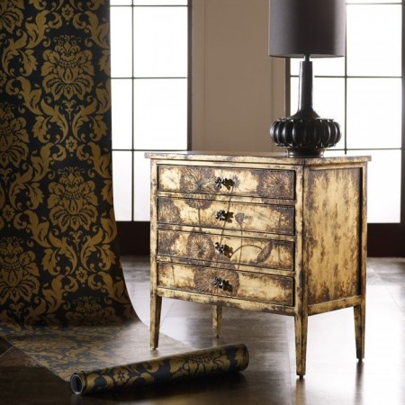 A shimmering gold and black dresser with a lustrous lamp in front of it.