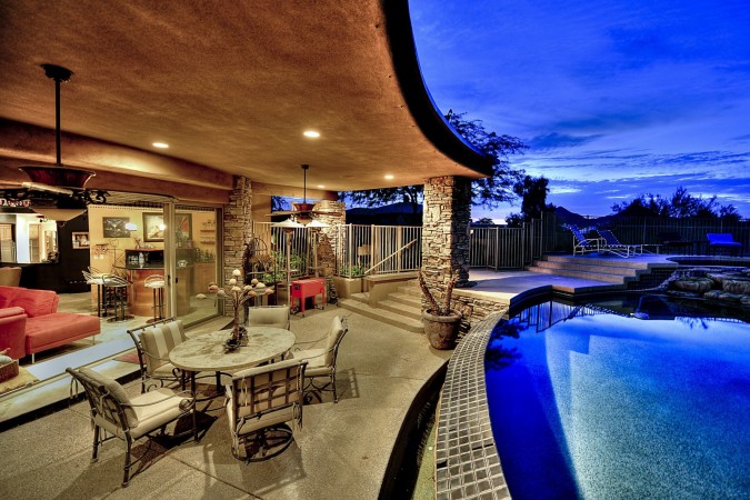 A luxury home with a pool and patio at dusk featuring indoor-outdoor rooms.