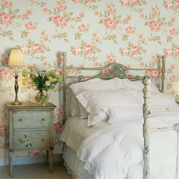 A bedroom with a bed and a bedside table featuring floral wall designs.