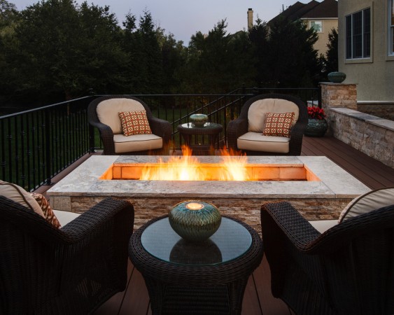 A fire pit on a deck with wicker furniture that heats up your backyard landscape.