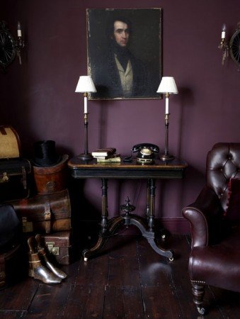 A room with dark purple walls and a moody painting on the wall.
