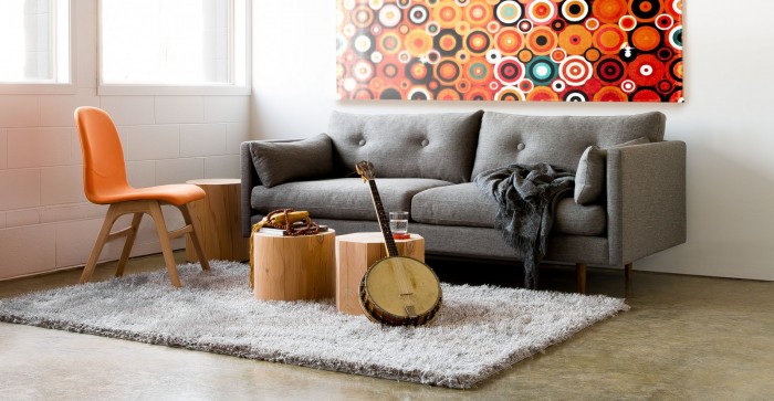 A living room with a gray couch and orange chair featuring natural-inspired tree trunk furniture pieces.
