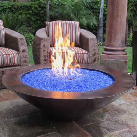 A fire pit with blue glass heating up a backyard landscape.