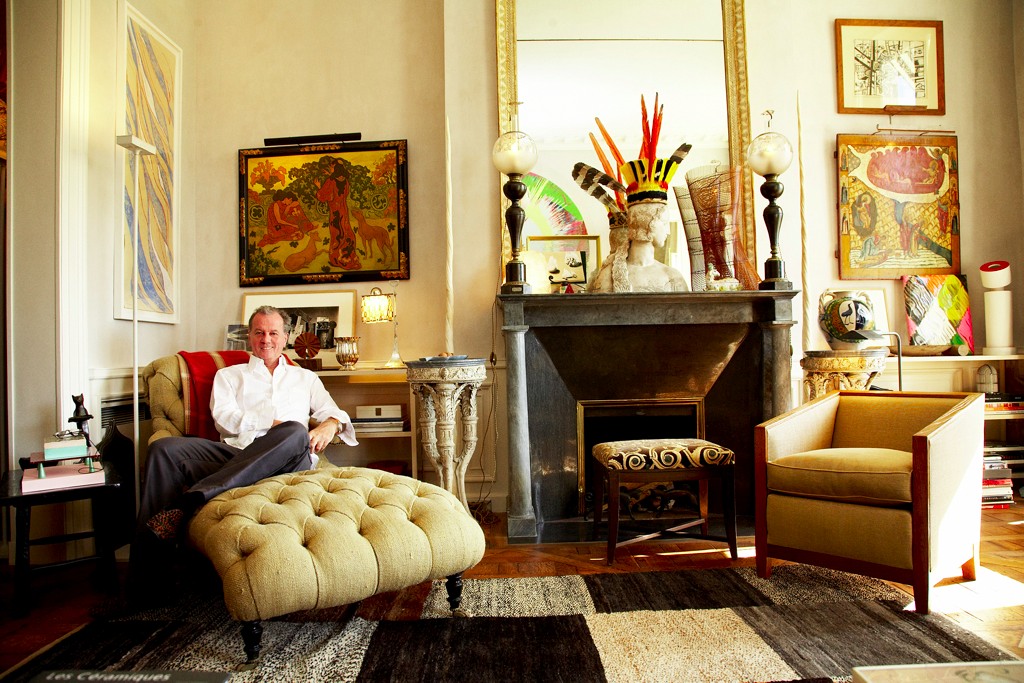 A man sitting in a chair in a living room showcasing Jacques Grange's designer focus.