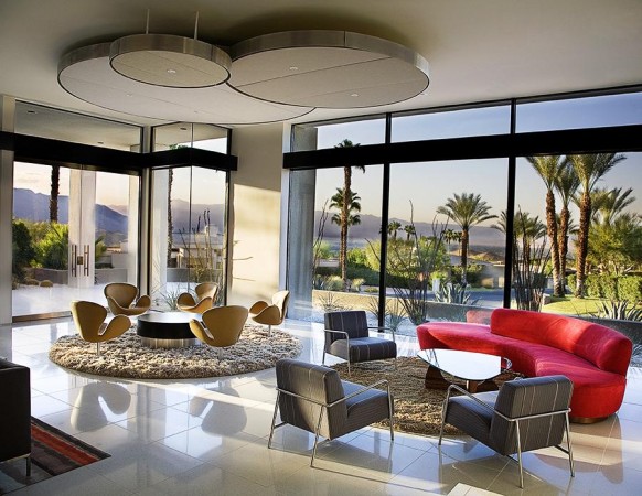 A living room with large windows and a red couch, showcasing mid-century modern glamour.