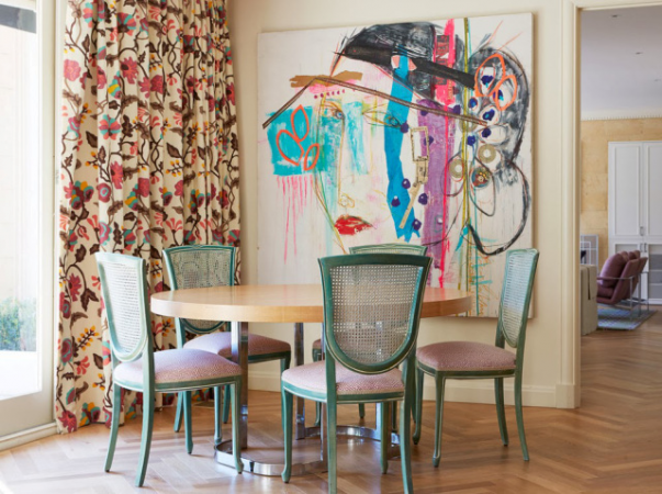 A dining room with an abstract colorful painting on the wall.
