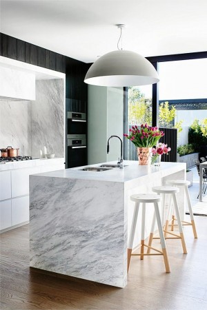 A modern kitchen with a marble island featuring waterfall countertops.