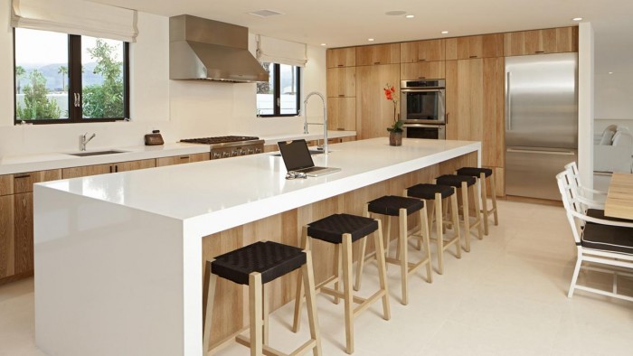 A modern kitchen with wooden waterfall countertops and stools.