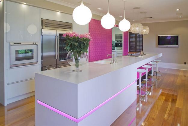 A modern white kitchen with vibrant pink lighting and stylish bar stools, adding character and color.
