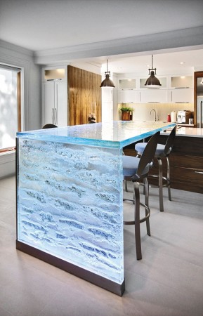 A kitchen with a glass countertop featuring waterfall kitchen countertops and bar stools.