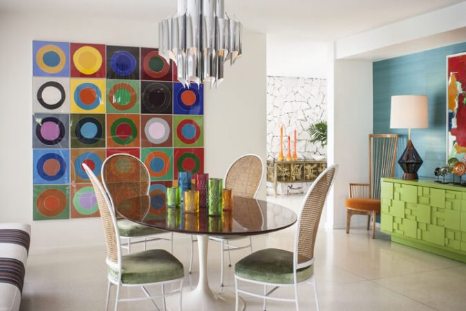 A colorful dining room with a sculptural painting on the wall.