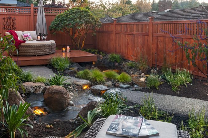 A backyard with a small stream and a wooden fence, perfect for creating a relaxing retreat.