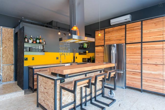 A modern kitchen with wooden cabinets and a bar stools, converted from a garage.