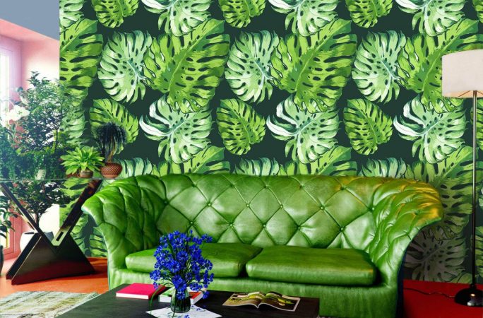 A living room with tropical vibes, featuring a green couch and green leaves on the wall.