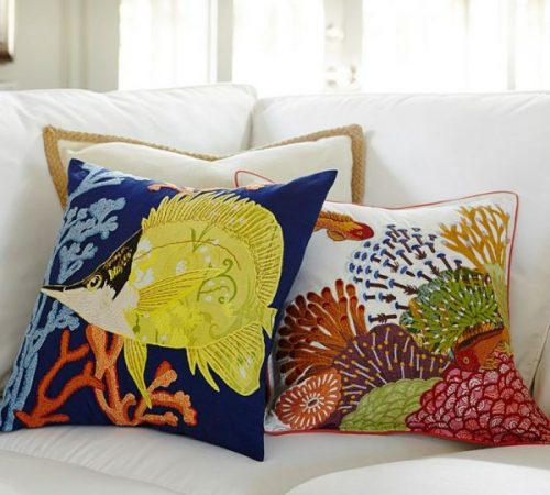 Two light pillows with tropical fish and corals on a white couch.