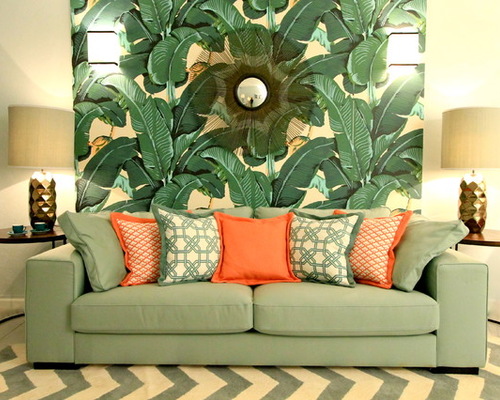 A living room with a tropical green and orange couch and a chevron wall.